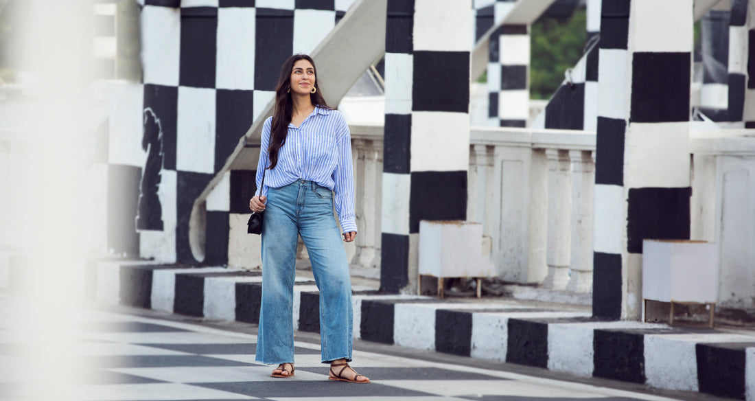 Image of a woman standing on a checkered bridge wearing a blue top and Go Colors Jeans.